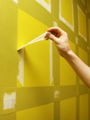 Hand peels masking tape away from painted yellow wall.